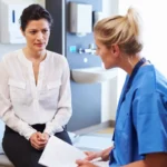 Female Patient And Doctor Have Consultation In Hospital Room